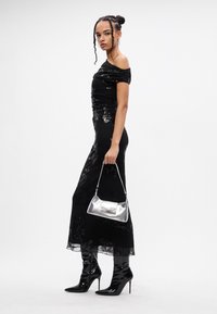 Melnas off-shoulder kleitas ar paildzinātiem akcentiem, pieguļošs siluets, caurspīdīga apakša, pāris ar sudrabu metālisku rokassomu un melnām augstpapēžu kurpēm.