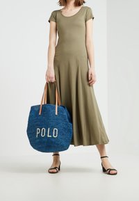 Abito verde oliva a maniche corte con orlo svasato. Una borsa a tracolla intrecciata blu con "POLO" in lettere crema e manici in pelle marrone. Sandali neri.