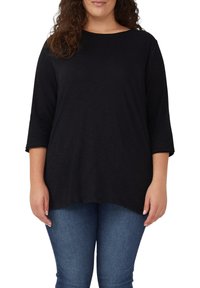 Zwart langevormig shirt met een relaxte pasvorm, ronde halslijn en zachte stof. Gecombineerd met denimblauwe jeans, wat een casual uitstraling geeft.