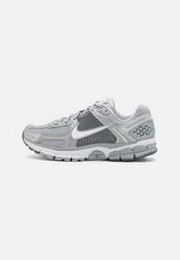 Šedá sportovní obuv vyrobená z prodyšné a syntetické látky. Má polstrovanou podrážku, aerodynamický design a výrazné bílé logo Nike.