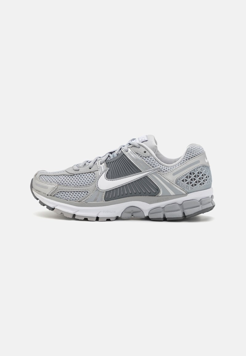 Šedá sportovní obuv vyrobená z prodyšné a syntetické látky. Má polstrovanou podrážku, aerodynamický design a výrazné bílé logo Nike.