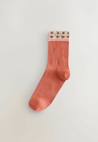 Ponožka farby hrdze s lemom so vzorom v krémovej, námorníckej modrej a oranžovej farbe. Vyrobená z mäkkého, textúrovaného materiálu s klasickým tvarom.