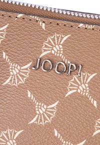 Brun læderpung med prægede lys beige mønstre og sølv "JOOP!" logo. Har en tekstureret overflade og lynlås lukning.