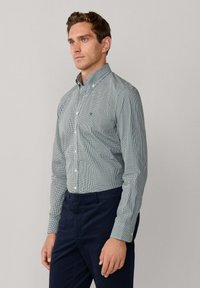 Camisa de manga larga a cuadros verdes y blancos con cuello abotonado, que presenta un pequeño logo bordado en el pecho y puños con botones.