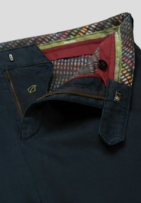 Navyblauwe broeken van een gestructureerde stof, met een gouden rits en een multicolor gevoerde binnenkant met rode en groene accenten.