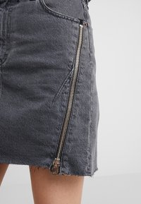 Šedá denimová sukně s roztrhaným lemem, která má výrazný boční zip a minimální švy.