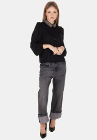 Blusa nera con bottoni e colletto decorato con perline, abbinata a jeans grigi in denim arrotolati e tacchi alti neri. Tessuto morbido e vestibilità comoda.