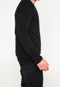 Zwarte lange mouwen trui met een geribde ronde halslijn en boorden. De stof lijkt zacht, met een getailleerde silhouet en een eenvoudig ontwerp.