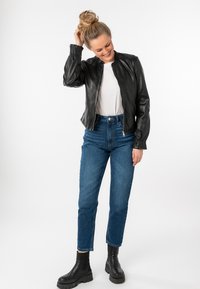 Zwarte leren bomberjack met rits, blauwe hoogwaistjeans en zwarte enkellaarzen, model met een casual kapsel.