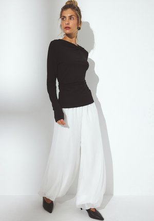 Black long-sleeve top with a draped design, paired with white wide-leg trousers, and black pointed-toe shoes. Smooth textures and contrasting colors.