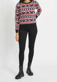 Stickad tröja med ett mönster i röd, vit och marinblått som visar renar och träd. Kombinationen med svarta skinny jeans och svarta ankelstövlar.