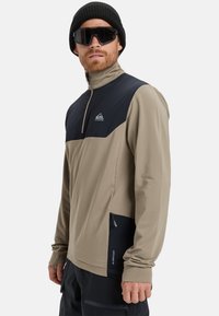 Letvægts zip-jakke i beige og sort. Tekstil med struktureret stof og en kontrasterende glat øverste sektion, frontlynlås og sidelomme med lynlås.