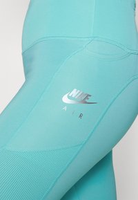 Zbliżenie na turkusowe legginsy sportowe z teksturowanymi panelami i srebrnym logo Nike Air na udzie.