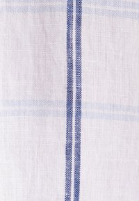 Gros plan d’un tissu blanc tissé avec deux bandes verticales bleues et de délicates lignes horizontales bleu clair en arrière-plan.