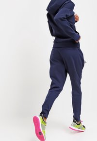 Marinblå hoodie och sweatpants set i mjukt material, med avslappnad passform. Träningsskor med gröna accenter och rosa sulor.