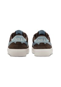 Brune ruskind sneakers med lyseblå accenter, hvid sål og "NIKE" logo på bagsiden. Har kontrastsyninger og en tekstureret overflade.