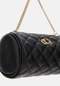 Czarna cylindryczna torba z pikowanej skóry z złotym łańcuchem i okrągłym złotym zapięciem z przodu.