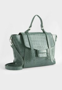 Sacoche en cuir texturé crocodile vert avec poignée supérieure, rabat avant, sangle latérale et bandoulière amovible sur fond blanc.