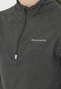 Nahaufnahme eines dunkelgrauen Viertel-Reißverschluss-Sportoberteils mit weißem "ENDURANCE"-Logo auf der Brust, das Nähte und Reißverschlussdetails zeigt.