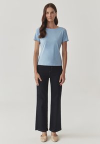 Top scurt de culoare bleu deschis, cu mânecă scurtă, combinat cu blugi evazați de culoare închisă, având o textură de material neted și balerini bej cu detalii cu curea.
