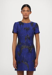 Zils ziedu kleita ar strukturētu audumu, īsām piedurknēm un pieguļošu siluetu ar melniem akcentiem un apaļu kakla izgriezumu.