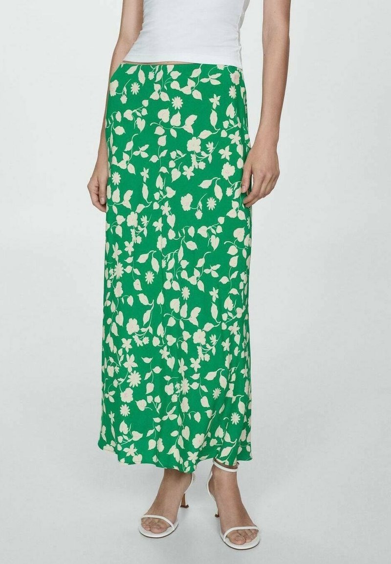 Gonna maxi verde con motivi floreali bianchi a foglia e fiore, dal design fluido e in tessuto leggero. Abbinata a sandali bianchi.