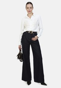 White shirt with floral embroidery, dark blue wide-leg jeans, black pointy-toed heels, and a small black handbag. Classic casual outfit.