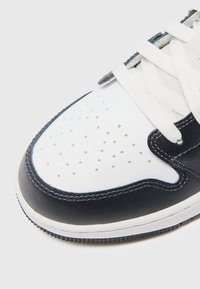 Gros plan sur l'avant d'une sneaker blanche et noire avec des perforations, des lacets blancs et des coutures détaillées sur une cuir lisse.