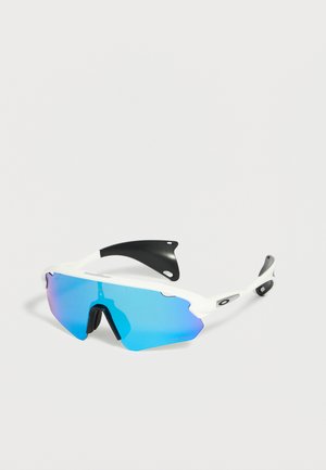 Occhiali da sole sportivi bianchi con una singola lente specchiata blu e naselli neri su uno sfondo chiaro e uniforme.