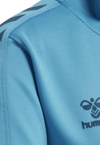 Light blue fabric with black hummel logo and chevron patterns on shoulder stitching of athletic wear.