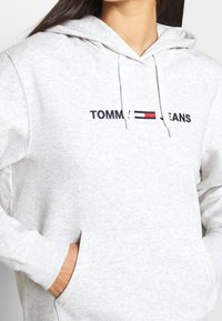 Grijze katoenen hoodie met een voorste kangoeroezak, voorzien van een geborduurd "TOMMY JEANS" logo in zwart, rood en blauwe horizontale strepen over de borst.