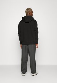 Felpa nera con cappuccio dal taglio rilassato, abbinata a pantaloni grigi a gamba larga. L'outfit presenta un tessuto testurizzato e polsini a coste.