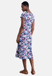 Floral pattern dress in blue, red, and white, featuring short sleeves, a fitted bodice, and a flowy A-line skirt. Worn with brown sandals.