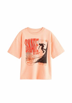 Persiko spalvos medvilninė T-marškinė su trumpomis rankovėmis, turinčios grafikos atvaizdą su riedlentininku, ryškų užrašą "SKATE" ir sluoksniuotas tekstūras.