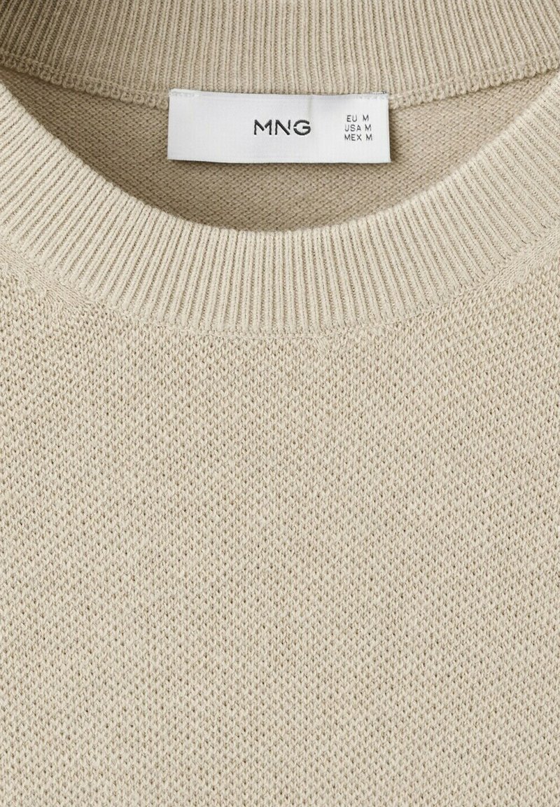 Pull beige en maille avec encolure ronde côtelée et étiquette blanche indiquant la marque MNG et la taille moyenne pour l'UE, les États-Unis et le Mexique.