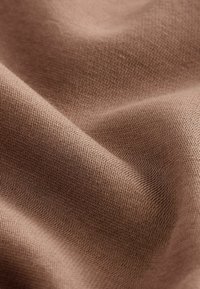 Tejido de punto marrón con una textura suave, creando ondas suaves y fluidas. El patrón de tejido es estrecho, mostrando un color rico y uniforme.