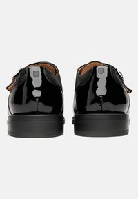 Schwarze Lacklederschuhe mit glatter Oberfläche und runden Zehen. Mit einer kleinen Schlaufe und einem Schnallenakzent an der Seite. Gummisohlen.