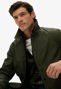 Jasnozielona, lekka kurtka z wysokim kołnierzem, z przodu na zatrzaski i z bocznymi kieszeniami. Nosi się ją na koszuli w kratę; gładka tekstura.