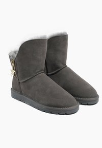 Botas de tobillo de ante gris con suave forro de piel de oveja gris, un acento dorado en forma de estrella en el lateral y una suela de goma para mayor tracción.