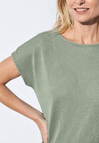 Grünes Kurzarmoberteil aus weichem Stoff, mit rundem Ausschnitt und lässiger Passform, sichtbaren Texturen und Nähdetails.