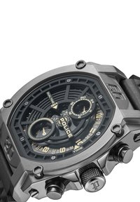 Ura iz nerjavečega jekla s črnim teksturiranim številčnico. Ponaša se z dvojnim prikazom časa, tremi podštevilčnicami in črnim gumijastim paskom. Prisotni so zlati poudarki.