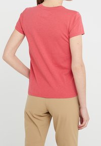 Krátký rukáv korálové tričko s kulatým výstřihem a hladkou texturou, kombinované s béžovými kalhotami, vytvářející uvolněný vzhled.