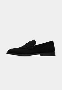 Svarta slip-on-skor med en slät överdel i tyg, rund tå, platt sula och en minimalistisk design med dubbelspänne.