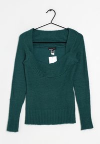 Pull sarcelle avec un large col côtelé et des manches longues. Fabriqué en matière douce, avec des poignets et un bas côtelés, suspendu à un crochet noir.