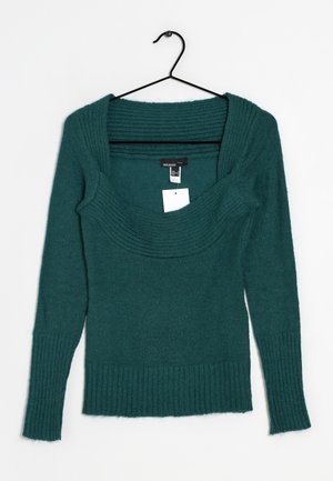Pull sarcelle avec un large col côtelé et des manches longues. Fabriqué en matière douce, avec des poignets et un bas côtelés, suspendu à un crochet noir.