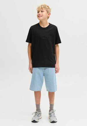 Camiseta de algodón negra con "ORIGINALS" impreso en una fuente sutil, combinada con pantalones cortos de mezclilla azul claro, calcetines grises y zapatillas deportivas grises.