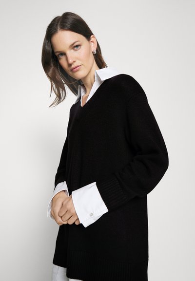 Schwarzer, lässig geschnittener Strickpullover mit V-Ausschnitt, ausgestattet mit gerippten Bündchen und Saum, kombiniert mit einem weißen Hemd mit Kragen. Sanfte Textur, lässiges Design.