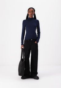 Haut à manches longues marine à col haut, design ajusté. Pantalons larges noirs, grand sac fourre-tout noir, chaussures noires chunky, accessoires simples.
