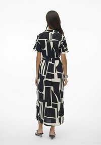 Vestido maxi estampado con mangas cortas. Presenta un diseño geométrico abstracto en blanco y negro. Cintura con cinturón, tejido fluido y longitud hasta el tobillo.