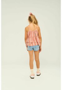 Persikofärgad och vit randig peplumtop med tunna remmar, kombinerad med ljusa denimshorts. Notabla detaljer: lagerdesign och lös passform.